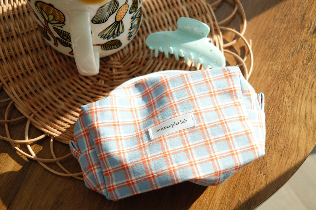 Twinkle Claw Clip in Light Blue, with Picnic Check Makeup Bag in Light Blue Check, styled on rattan